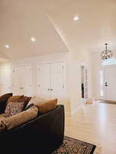 Living room featuring lofted ceiling, light wood-type flooring, and a notable chandelier