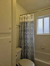 Bathroom with toilet and shower / bathtub combination with curtain