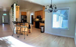 Kitchen featuring hanging light fixtures, stainless steel appliances, tasteful backsplash, a notable chandelier, and light wood-type flooring