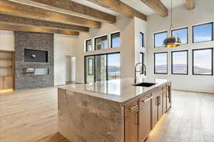 Kitchen with a fireplace, an island with sink, beamed ceiling, and sink