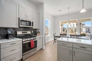 Kitchen with stainless steel appliances, an inviting chandelier, tasteful backsplash, light hardwood / wood-style floors, and pendant lighting