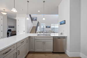 Kitchen with sink, hanging light fixtures, stainless steel dishwasher, light hardwood / wood-style floors, and kitchen peninsula