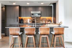 Kitchen featuring decorative backsplash, light wood-type flooring, dark stone counters, and a breakfast bar area