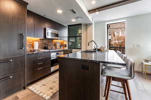 Kitchen with a kitchen island with sink, sink, a breakfast bar area, beam ceiling, and stainless steel appliances