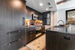 Kitchen with appliances with stainless steel finishes, dark brown cabinets, dark stone counters, and sink