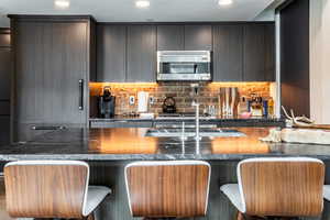 Kitchen featuring a center island, electric cooktop, dark stone countertops, tasteful backsplash, and a kitchen bar