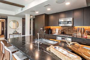 Kitchen featuring sink, appliances with stainless steel finishes, tasteful backsplash, a kitchen bar, and dark brown cabinetry