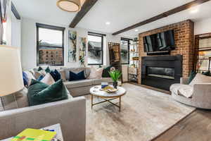 Living room featuring beam ceiling, wood-type flooring, and a brick fireplace