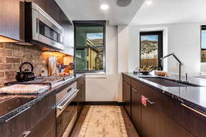 Kitchen with sink, dark brown cabinetry, stainless steel appliances, and tasteful backsplash