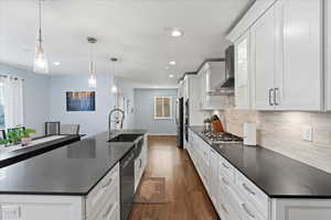 Kitchen with appliances with stainless steel finishes, wall chimney exhaust hood, pendant lighting, white cabinets, and dark hardwood / wood-style floors