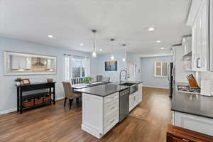 Kitchen featuring pendant lighting, wall chimney range hood, sink, white cabinetry, and stainless steel appliances