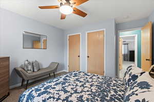 Carpeted bedroom with ceiling fan and two closets