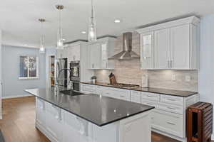 Kitchen featuring appliances with stainless steel finishes, a center island with sink, white cabinetry, and wall chimney exhaust hood