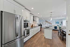 Kitchen featuring dark wood-type flooring, white cabinets, hanging light fixtures, wall chimney exhaust hood, and stainless steel appliances