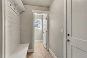 Mudroom featuring light wood-type flooring, shiplap wall, bench, and hooks