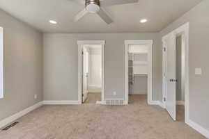 Unfurnished bedroom featuring ensuite bath, ceiling fan, a spacious closet, and light colored carpet