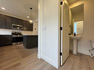 Kitchen with light wood-type flooring, dark brown cabinetry, stainless steel appliances, sink, and hanging light fixtures