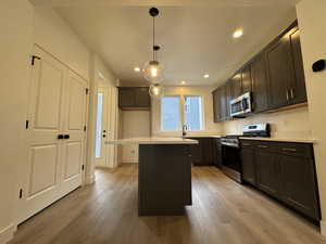 Kitchen with a kitchen island, stainless steel appliances, decorative light fixtures, and light wood-type flooring