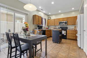 Kitchen featuring light tile patterned flooring, hanging light fixtures, a center island, and black appliances