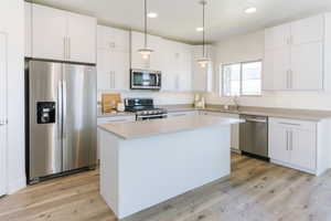 Kitchen featuring white cabinetry, hanging light fixtures, and appliances with stainless steel finishes