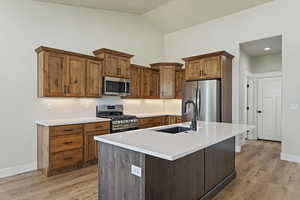 Kitchen with appliances with stainless steel finishes, a kitchen island with sink, sink, light hardwood / wood-style floors, and lofted ceiling