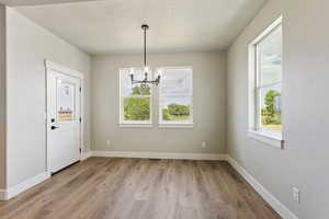 Unfurnished dining area featuring light hardwood / wood-style floors, a textured ceiling, and an inviting chandelier