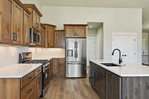 Kitchen featuring sink, light wood-type flooring, an island with sink, and appliances with stainless steel finishes