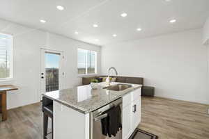 Kitchen featuring light stone countertops, dishwasher, sink, an island with sink, and white cabinets