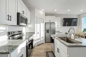 Kitchen with stone counters, sink, an island with sink, white cabinetry, and stainless steel appliances