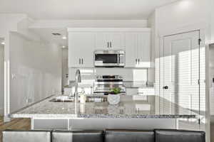 Kitchen featuring light stone countertops, white cabinetry, sink, and appliances with stainless steel finishes