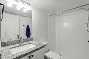 Bathroom with a shower, vanity, a textured ceiling, and toilet