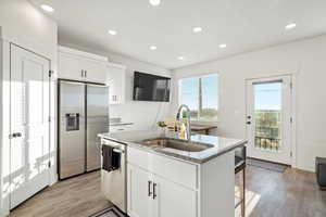 Kitchen featuring light stone counters, stainless steel appliances, sink, white cabinetry, and an island with sink