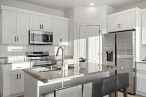 Kitchen featuring white cabinets, light stone countertops, and stainless steel appliances