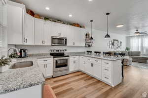 Kitchen with kitchen peninsula, appliances with stainless steel finishes, sink, white cabinets, and hanging light fixtures