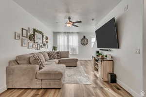 Living room with ceiling fan, a textured ceiling, and light hardwood / wood-style flooring