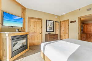 Bedroom with a multi sided fireplace and light carpet