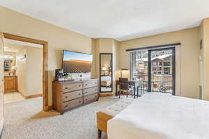 Bedroom featuring light carpet, a textured ceiling, ensuite bathroom, and access to exterior