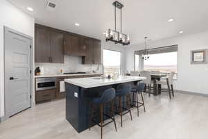 Kitchen with premium range hood, dark brown cabinetry, gas stovetop, built in microwave, and a kitchen island with sink