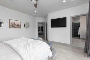 Bedroom with ensuite bath, light hardwood / wood-style floors, a spacious closet, and ceiling fan