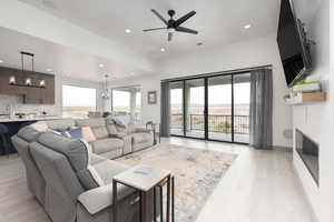 Living room with ceiling fan with notable chandelier, light wood-type flooring, and a healthy amount of sunlight