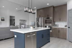 Kitchen with dark brown cabinetry, stainless steel appliances, tasteful backsplash, pendant lighting, and a kitchen island with sink