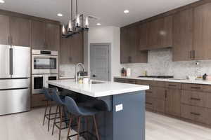 Kitchen with stainless steel appliances, backsplash, decorative light fixtures, a breakfast bar, and a center island with sink