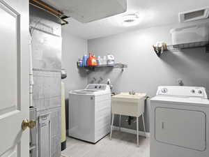 Laundry room featuring light wood-type flooring, separate washer and dryer, and sink