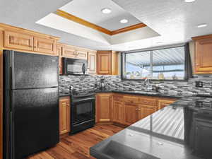 Kitchen with ornamental molding, a tray ceiling, sink, black appliances, and light hardwood / wood-style flooring