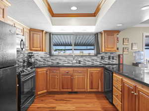 Kitchen featuring backsplash, crown molding, sink, black appliances, and light hardwood / wood-style flooring