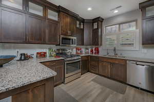 Kitchen with light stone counters, sink, stainless steel appliances, and light hardwood / wood-style flooring