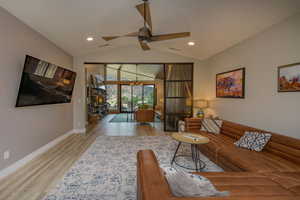 Living room featuring vaulted ceiling, ceiling fan with notable chandelier, and light wood-type flooring