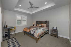 Carpeted bedroom with a raised ceiling and ceiling fan