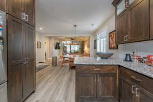 Kitchen featuring light stone counters, dark brown cabinetry, backsplash, and hanging light fixtures