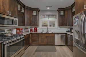 Kitchen with sink, tasteful backsplash, light stone counters, light hardwood / wood-style floors, and appliances with stainless steel finishes